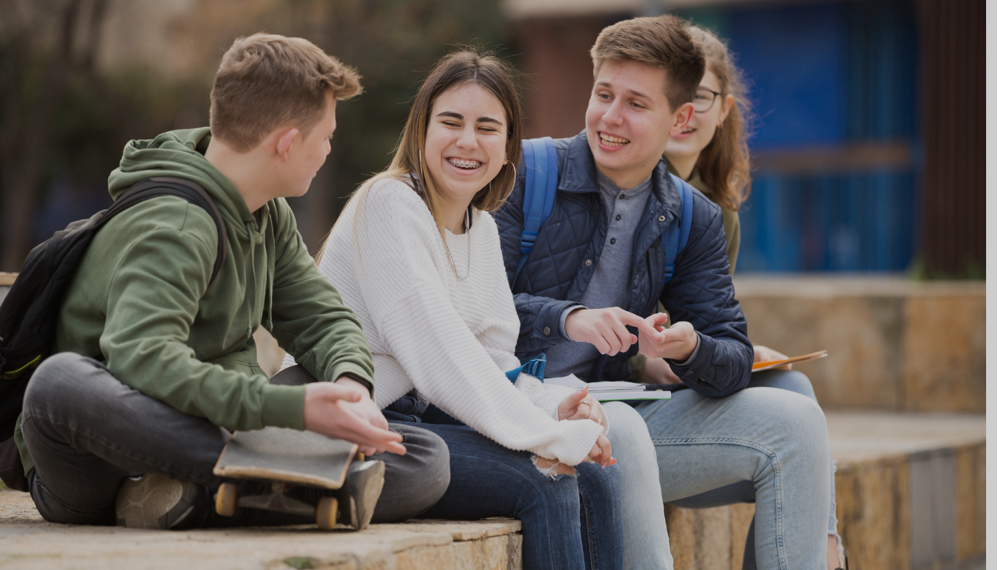 Group of laughing teens sitting on a wall outside
