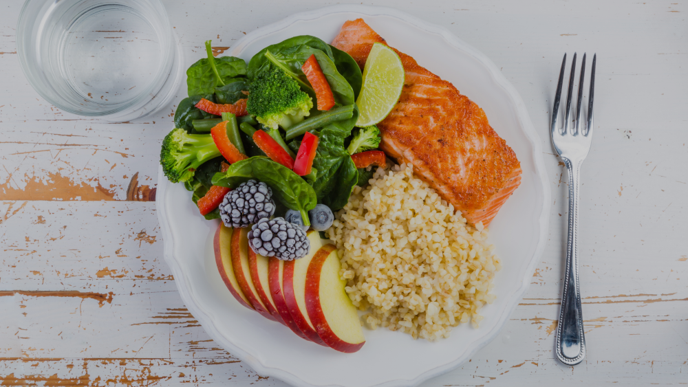 A healthy plate of salmon, rice, fruits and vegetables with a fork