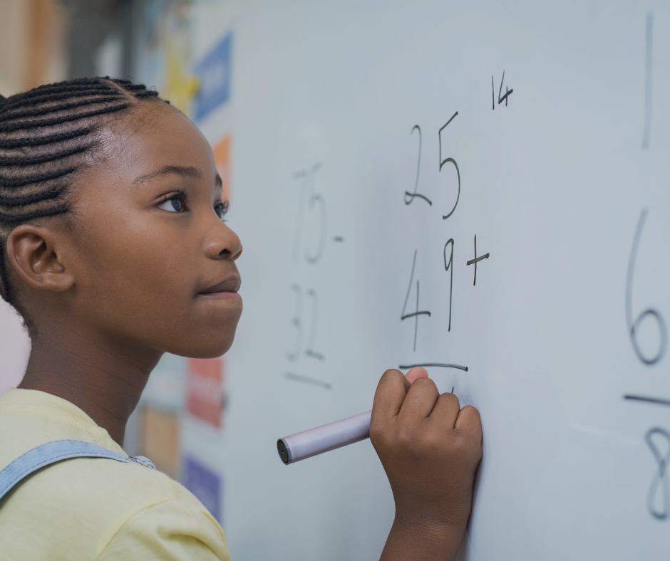 Primary aged girls solving math problems on a white board with a marker pen