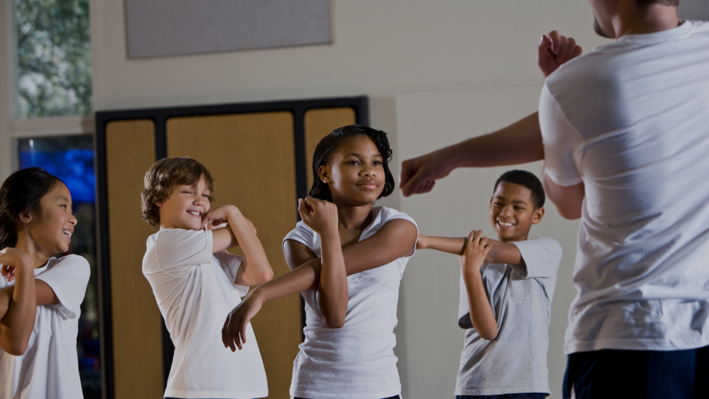 Group of primary school children stretching for a physical education lesson with their teacher