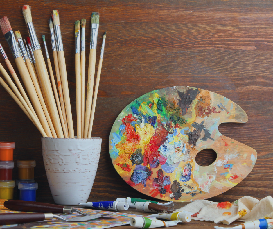 A large cup of paintbrushes and a very used color palette with paints