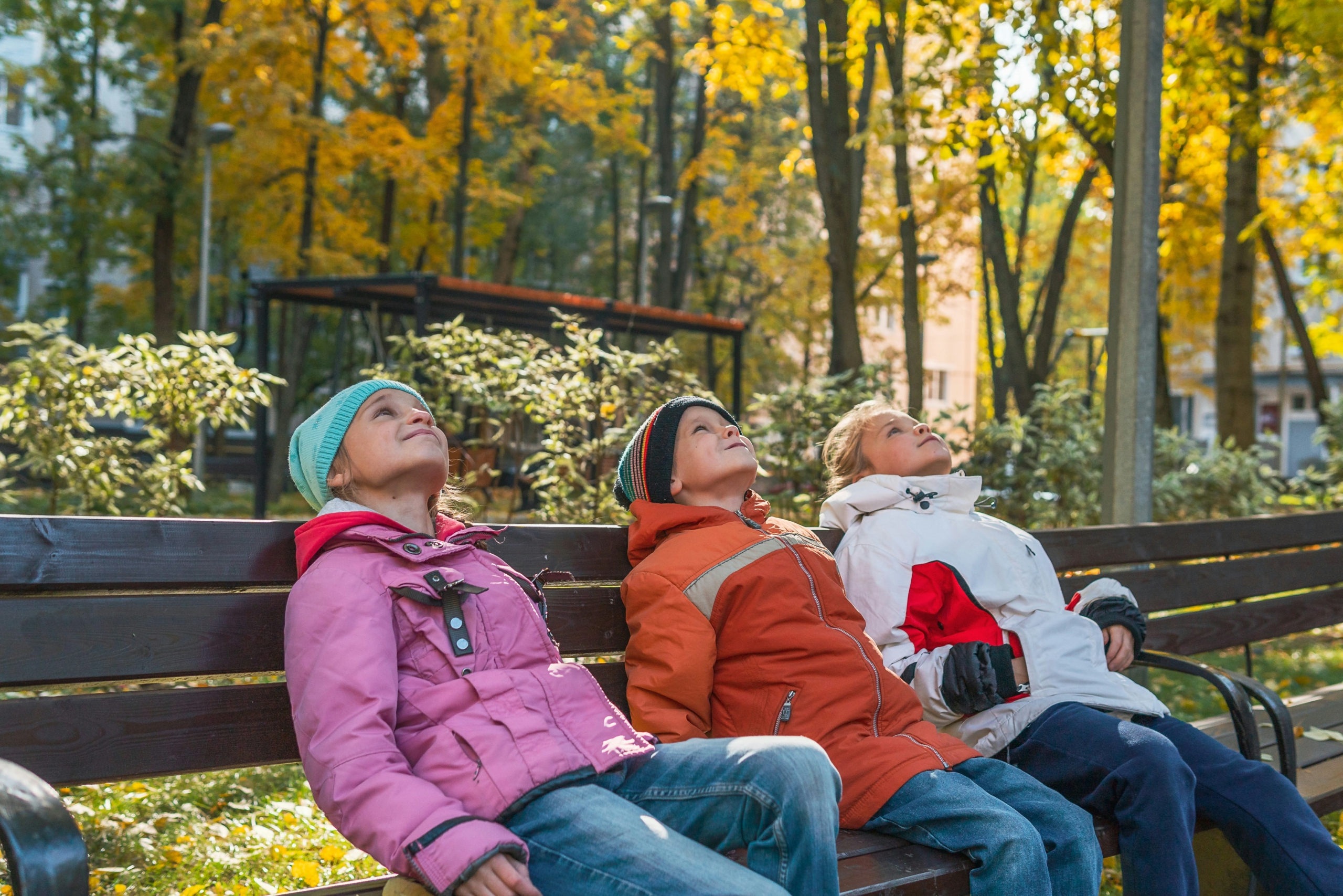 three girls looking up in to the sky sitting on a bench in the winter sunshine