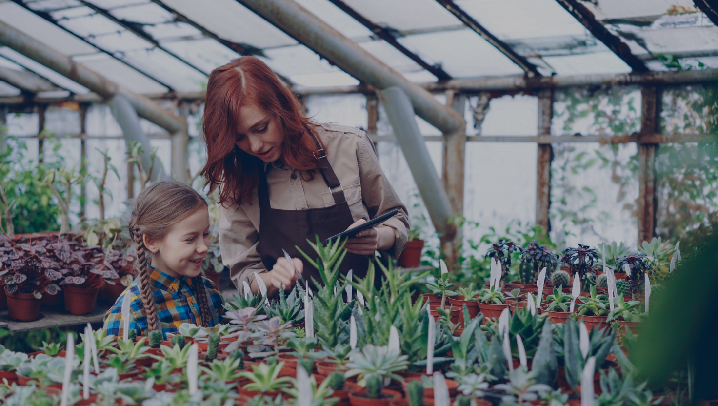 Female teacher showing a young girl plants in a greenhouse, outdoor learning